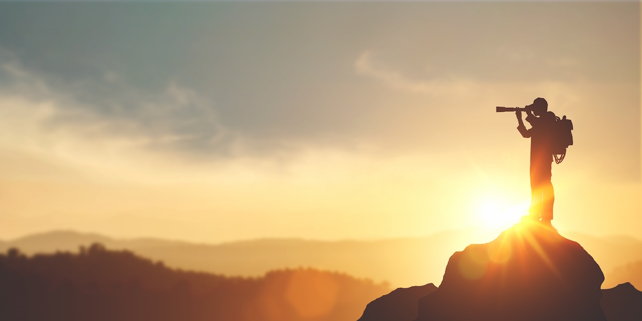 A silhouette of a person standing on a rocky peak at sunset